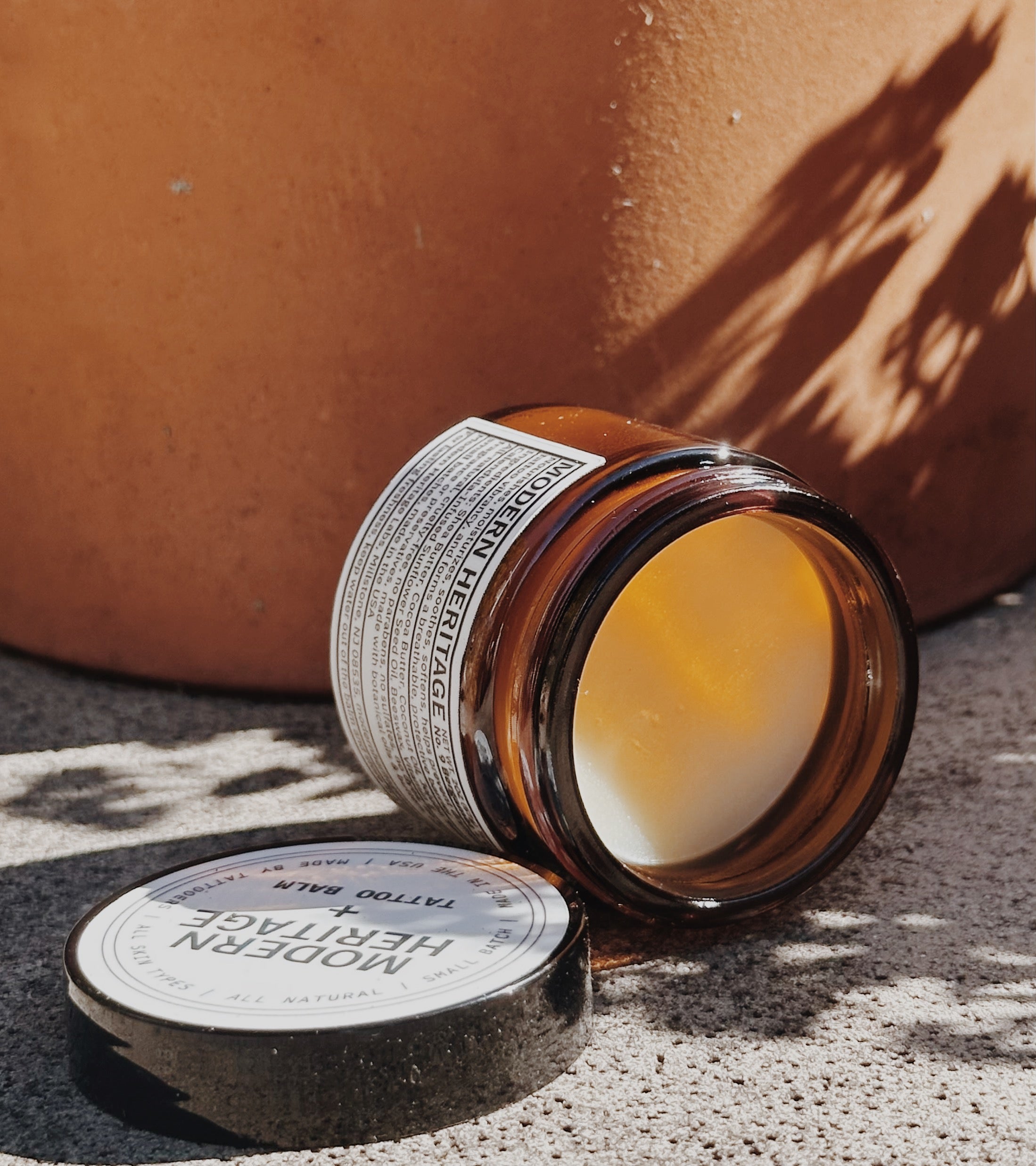 Open jar of Modern Heritage tattoo balm beside a terracotta pot