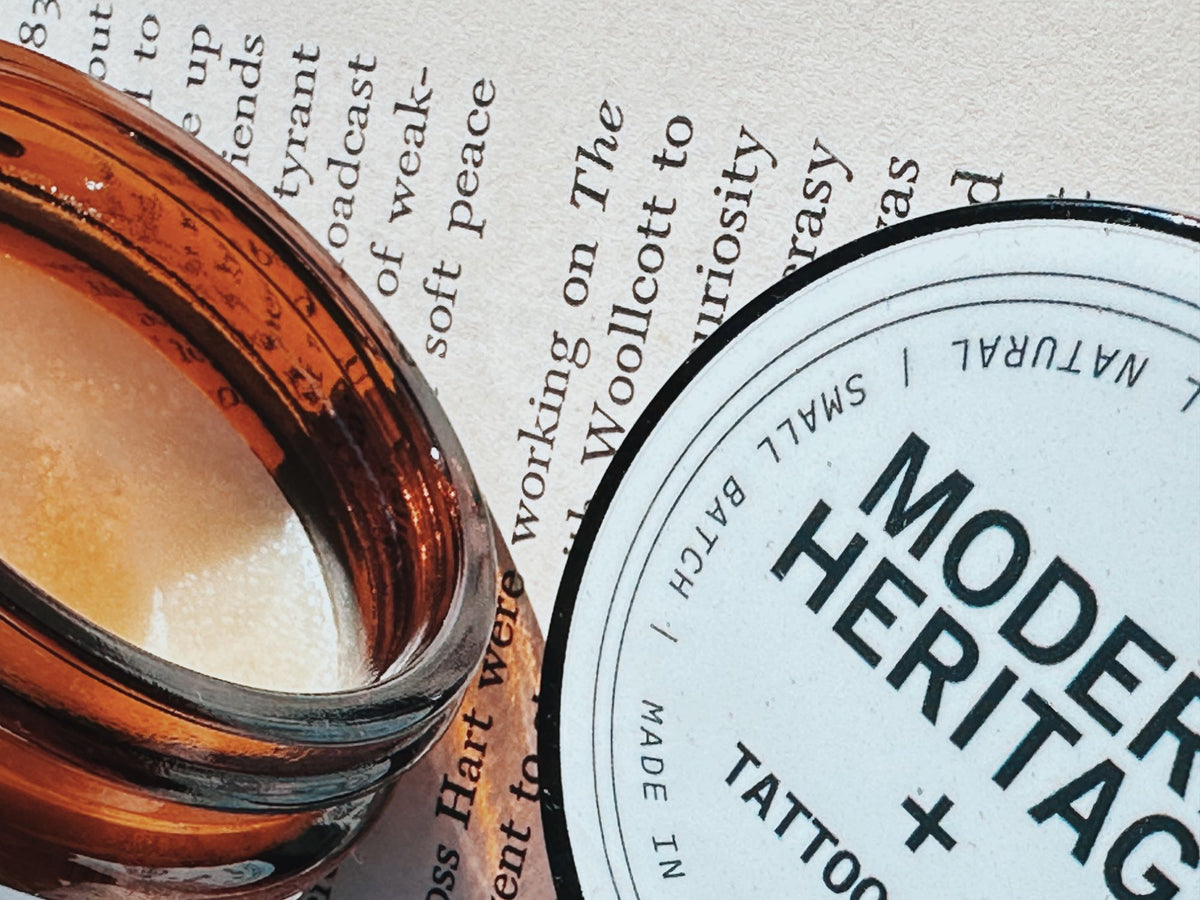 Modern Heritage tattoo balm jar and lid resting on an open book