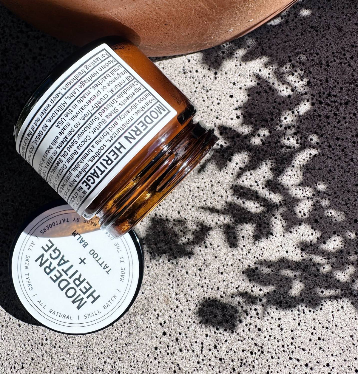 Modern Heritage tattoo balm jar tipped on concrete in dappled light