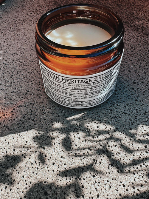 Open jar of Modern Heritage No. 9 Bergamot and Vetiver tattoo balm on sunlit concrete